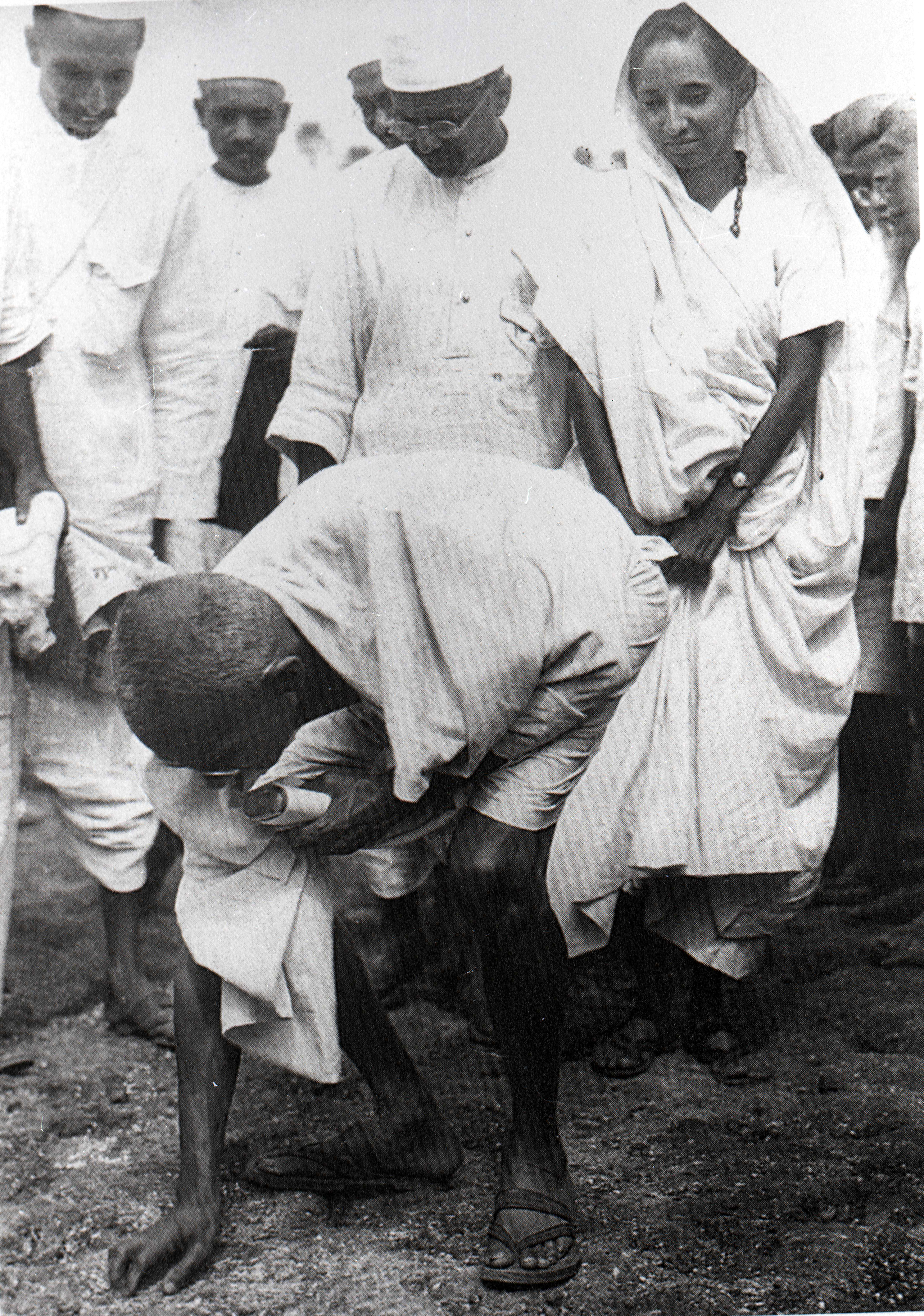 Mahatma Gandhi picking up salt at Dandi, with companions behind him.